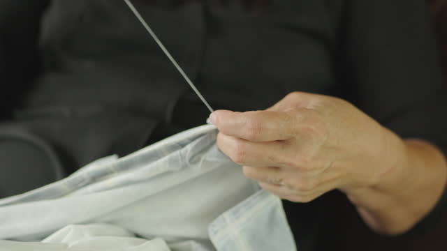 Closeup woman hands sewing and repairing button on shirt