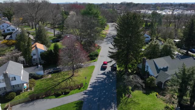 Red car on street in American suburb neighborhood. Sunny day in spring season. Aerial tracking shot.