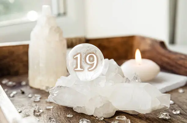 Number nineteen on gemstone sphere or crystal ball known as crystallum orbis or orbuculum. Natural clear quartz ball on stand on wood tray in home. Predictions concept.