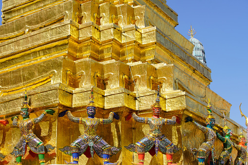 ramayana demon statue which support golden pagoda against blue sky at royal grand palace,bangkok,THAILAND.