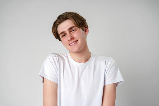 A young man clad in a white t-shirt smiles directly at the camera, exuding a sense of casual confidence. His friendly expression and relaxed posture make for a warm and inviting image.