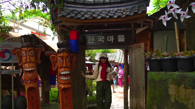 Traditional Korean village entrance with colorful wooden totems and a person posing under the gate.