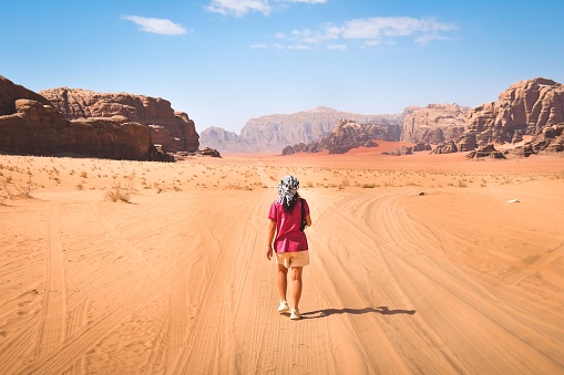 Adventure and explore in changed planet earth for climate warming concept - woman viewed from back walking on desert dunes with blue sky and wadi rum mars alike background