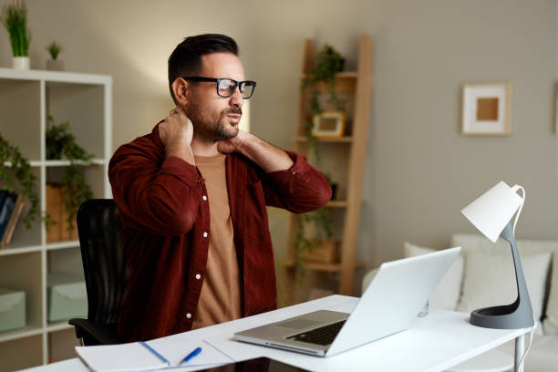 istock Young man has neck pain while working in the office at a desk 2132844600