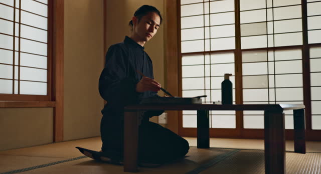 Man, calligraphy or creative Japanese artist in studio for art and script, letter with table, paper or painting. Writing, brush or person with tools, paintbrush and focus with traditional stationery