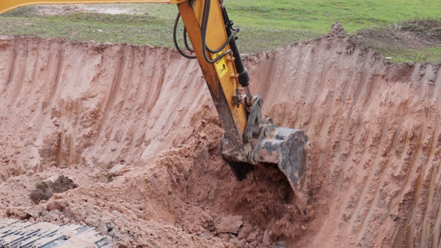 A large yellow and black excavator is digging into a muddy hillside