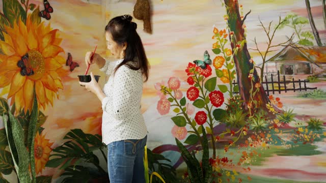 Mature woman painting a colorful mural on a wall at home