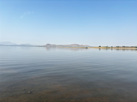 A calm lake with a mountain in the background. The sky is clear and blue. The water is still and peaceful
