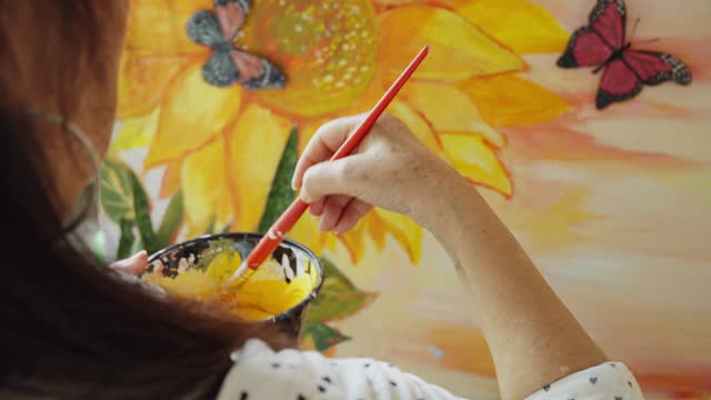Mature woman using a brush to paint a colorful mural at home