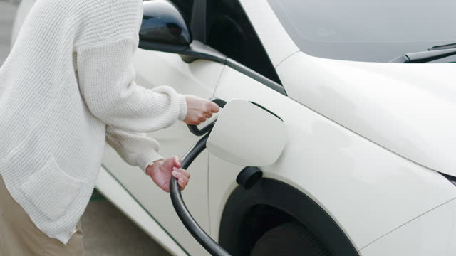 close up asian woman plug in charger in to ev car at electronic charging station