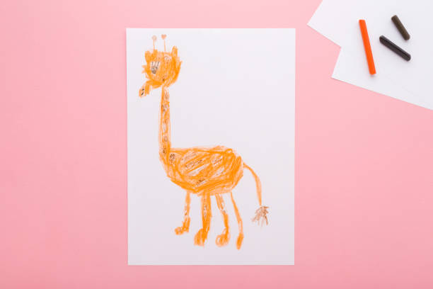 istock Drawn cute giraffe shape on white paper. Colorful wax crayons on light pink table background. Pastel color. Closeup. Children drawing art. Top down view. 2132916934