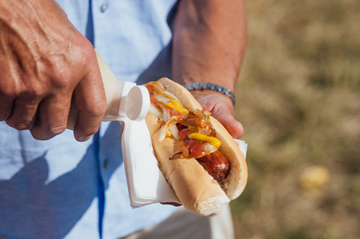 Close up of a man adding sauce to a hotdog while at a outdoor travelling carnival  in the North East of England.