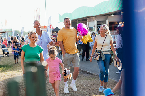 Multi generation family visiting an outdoor travelling carnival with different rides and food stalls in the North East of England. They are holding hands, walking side by side in the sunshine.