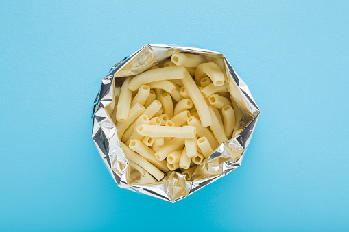 Opened foil bag of white potato chips sticks on light blue table background. Pastel color. Closeup. Top down view.