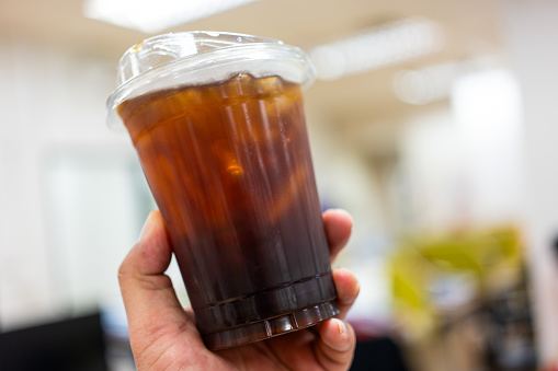 Iced black coffee or americano blend in plastic cup in hand. Close up