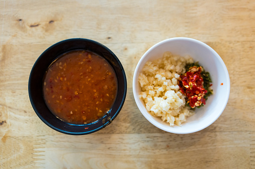 Sukiyaki dipping sauce with minced garlic and chilli in black bowl on wood table