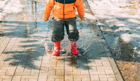 Gleeful Puddles : With every step, the child's red boots send a cascade of droplets into the air, a celebration of melting snow on a sunny day