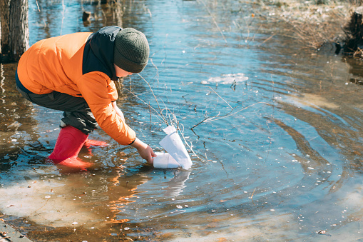 Springtime Sailor : Amid the budding trees, a young boy leans into the experience of launching a paper boat, symbolizing new beginnings and simple joys