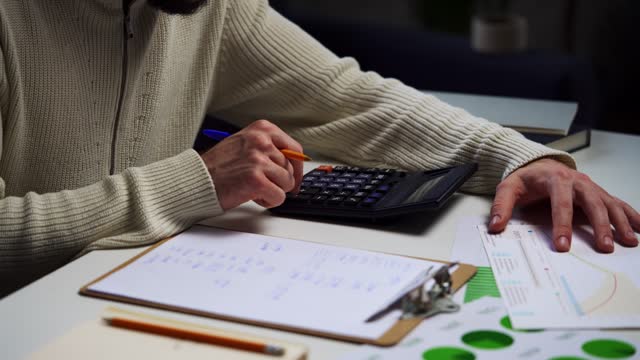 Man Calculating Budget With Calculator and Paperwork at Home Office Desk