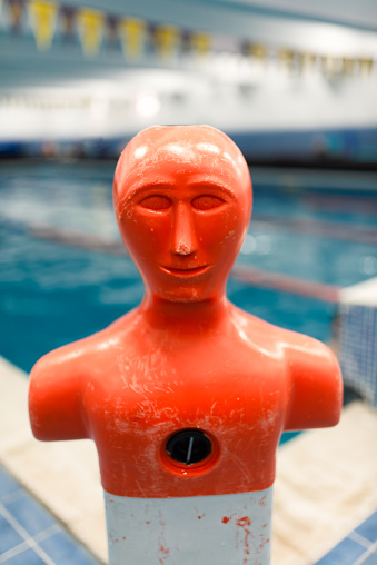 Portrait stock photo of a life saving practice dummy in front of indoors swimming pool