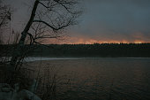 Calm lake at winter surrounded by forests. Dusk