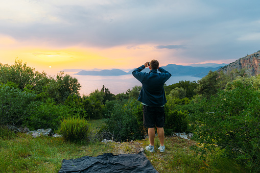 Rear view of a male photographing the Mediterranean sea with the hills of Oludeniz during dramatic colorful sunset in Mugla province, Middle East