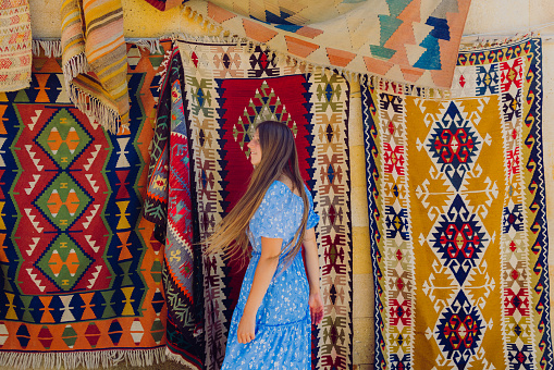 Side view of a happy female with long hair and in a blue dress walking by the colourful authentic Turkish carpets in the background in Göreme, Middle East