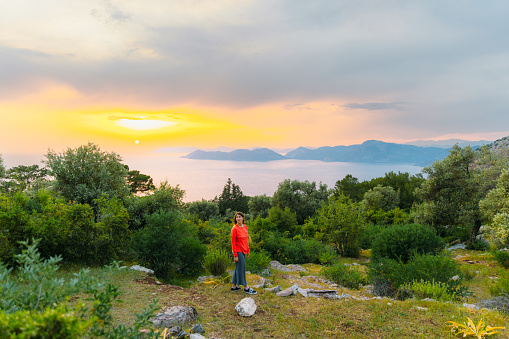 Happy female walking to the viewpoint of the Mediterranean sea with the hills of Oludeniz during dramatic colourful sunset in Mugla province, Turkey