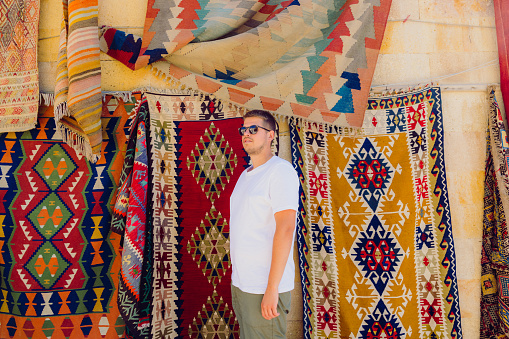 Side view of a male in sunglasses walking by the colourful authentic Turkish carpets in the background in Göreme, Middle East