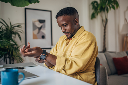 Focused black man in a casual shirt checks his smartwatch in a cozy, well-lit living room