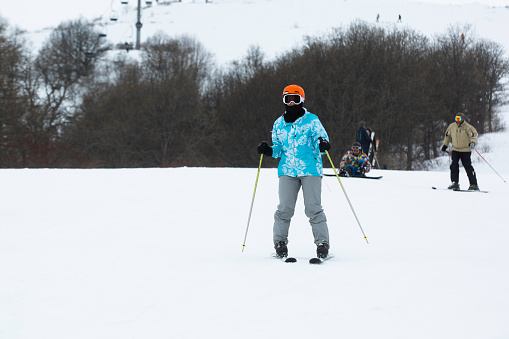 Tsakhkadzor, Armenia – December 14, 2023: A skier in a blue jacket cross-country skiing among trees on a snowy hill