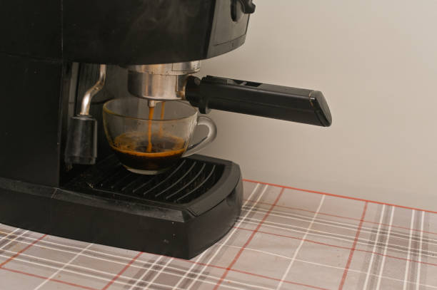 A coffee maker fills a glass cup with fragrant coffee