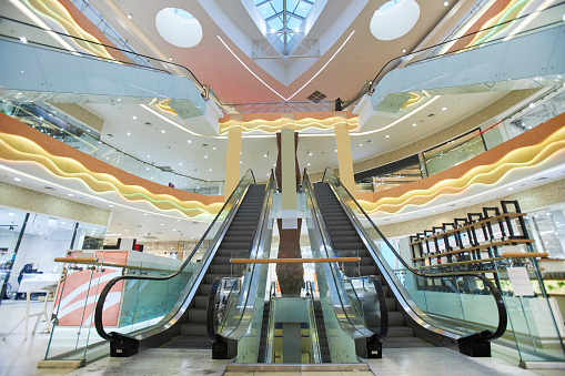 Dramatic wide angle view of shopping mall interior with focus on escalator stairs copy space