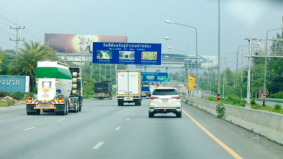 Driving on highway and passing welcome sign in Amphoe Pak Chong in Nakhon Ratchassima province in Thailand. A few traffic is ruling and huge banners are alongside highway including gas stations