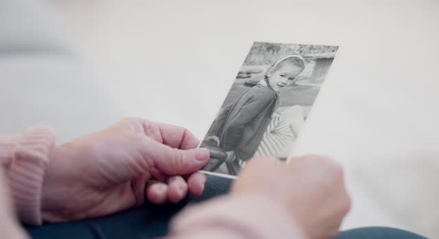 Senior woman, holding and photo with memory with hands and remembering a child in closeup. Retirement, history and elderly person with retro picture in home with nostalgia or thinking about past.