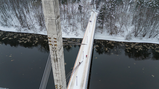 Drone photography of concrete footbridge covered by snow and pedestrians crossing during winter cloudy day