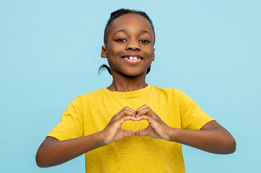 Friendly African American little boy showing heart made with hands isolated over blue background