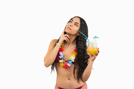 Pensive brunette Latin woman in bikini holding a orange soda with hand on face on white background