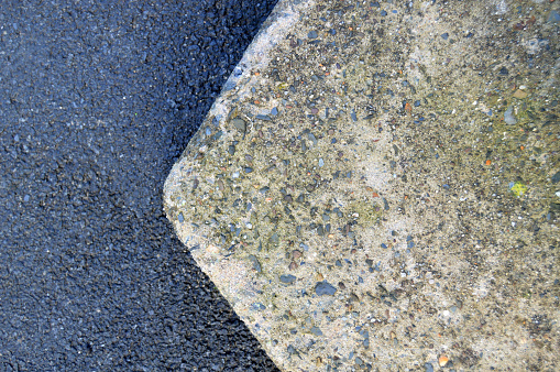 Gray coloured divided background with pebbles or gravel and black asphalt over horizontal backdrop with variety of small stones studded over textured rough rustic concrete surface. Left side is blurred, focus only on bright lighter concrete stones segregation.
