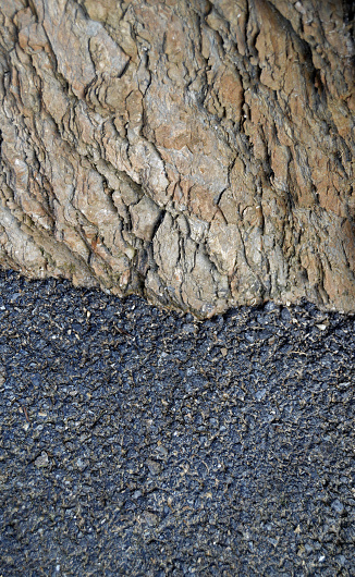 Gray coloured divided halved background with textured dark black asphalt on top half and contrasting rock or stone texture over top on a vertical backdrop making rough rustic hardened wall or wallpaper denoting strength, power.