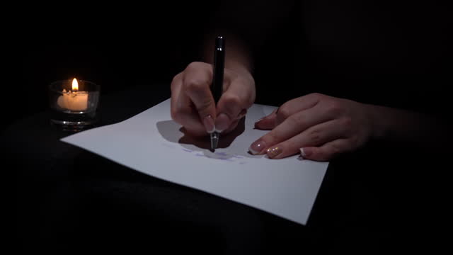 Hand Writes with a Pen on White Paper in a Dark Room by Candlelight