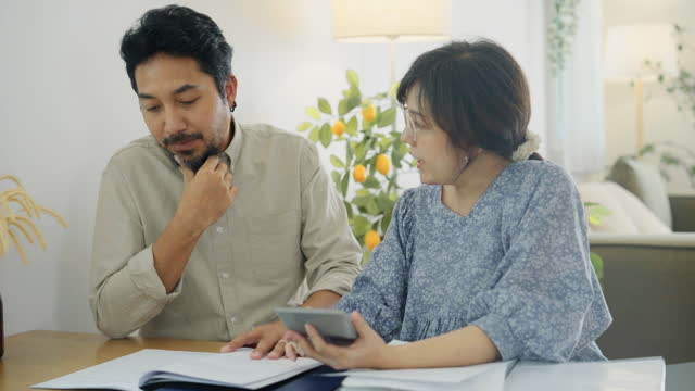 An Asian family manages finances by reviewing documents in the living room together.