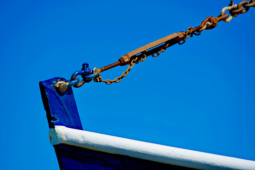 Close-up view of a steel chain with a turnbuckle attached to the bow of a commercial fishing trawler.