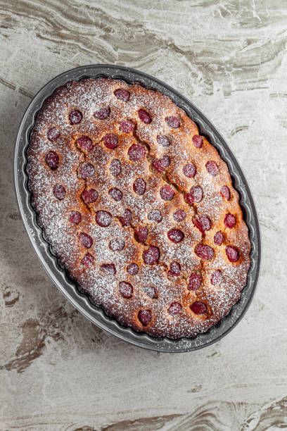 Delicious homemade peach clafoutis, an eggy custard baked with sweet summer fruit, a creamy texture with sliced peaches and icing sugar dressing in a plate, the most cherished home-baked desserts in France made with fresh peaches, vanilla extract,  sugar, lemon zest, eggs, milk, heavy cream, flour, ground cardamom, salt and dusted with icing sugar