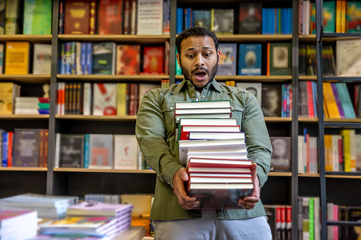 Library. Young african american man carrying a pile of books