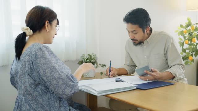 An Asian family manages finances by reviewing documents in the living room together.