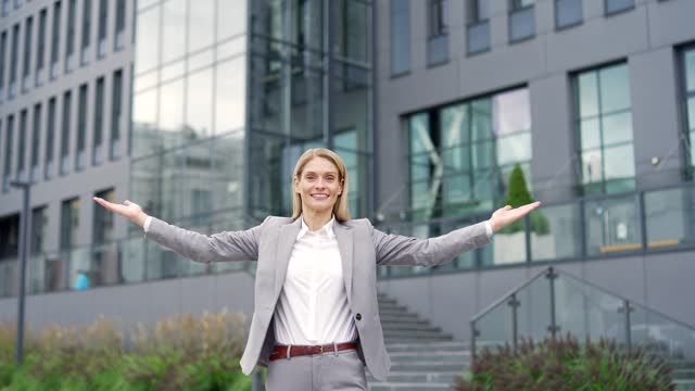 Confident happy businesswoman invites you to join team near entrance to business office building.