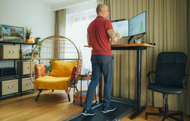 Man working from home at standing desk is walking on under desk treadmill