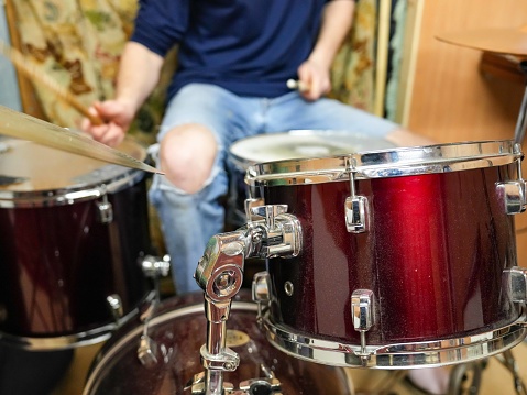 A cool musician sitting playing his drum kit. The Gen Z young man is enjoying practising his music. He is wearing torn jeans and casual clothing.