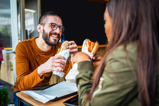Young cheerful couple eating and having fun in fast food restaurant